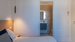 A hotel room with a bed, bedside lamp, and a view into the bathroom. - Stylish 2-Bedroom Stays near Colosseum (Rome)