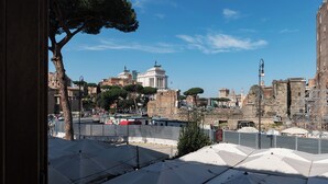 A view of ancient ruins with a clear sky, including a large tree and some modern structures in the foreground. - Stylish 2-Bedroom Stays near Colosseum (Rome)