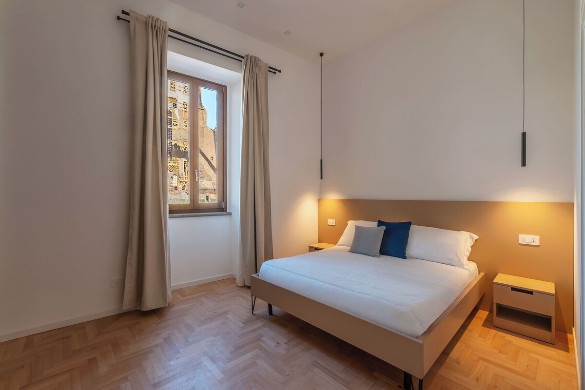 Ein modernes Schlafzimmer mit einem großen Bett, einem Nachttisch, einer Nachttruhe und einem Fenster mit Vorhängen.