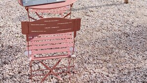 A laptop on a table with a chair, surrounded by gravel, with a wooden fence and flowering plants in the background. - Bed and breakfast, Besse sur Issole, Var. Ideal for a quiet, sunny stay (Besse-sur-Issole)