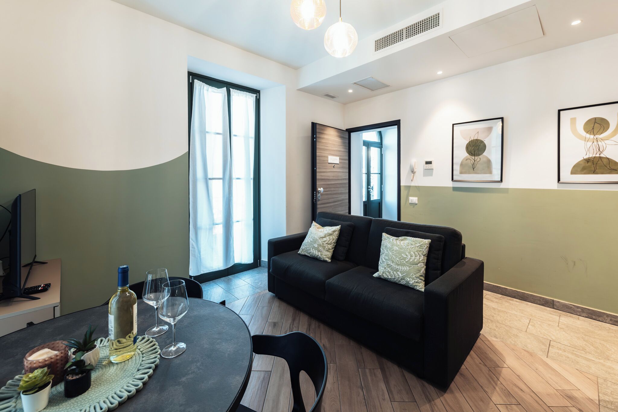 Ein modernes Wohnzimmer mit einer Couch, einem Esstisch mit Weingläsern und Kunstwerken an den Wänden.