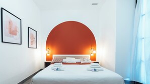 Une chambre d’hôtel moderne avec un grand lit, deux tables de chevet, une tête de lit blanche et des œuvres d’art encadrées accrochées aux murs.