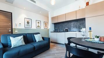 Una sala de estar moderna con un sofá azul oscuro, una mesa de comedor con sillas y una cocina con armarios y una encimera.