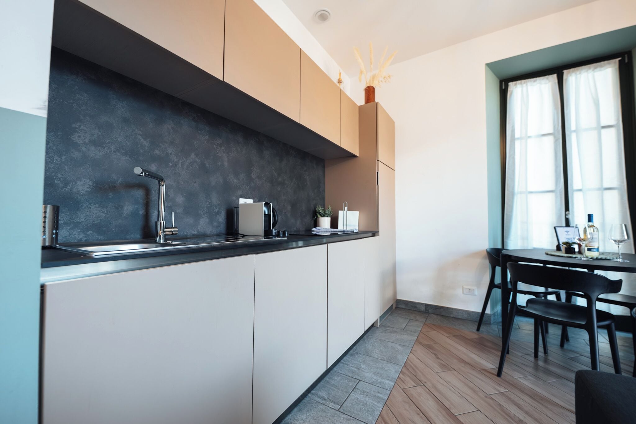 A modern kitchen with a dark backsplash, white cabinets, and a dining area with a table and chairs.