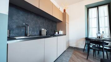 A modern kitchen with a dark backsplash, white cabinets, and a dining area with a table and chairs.