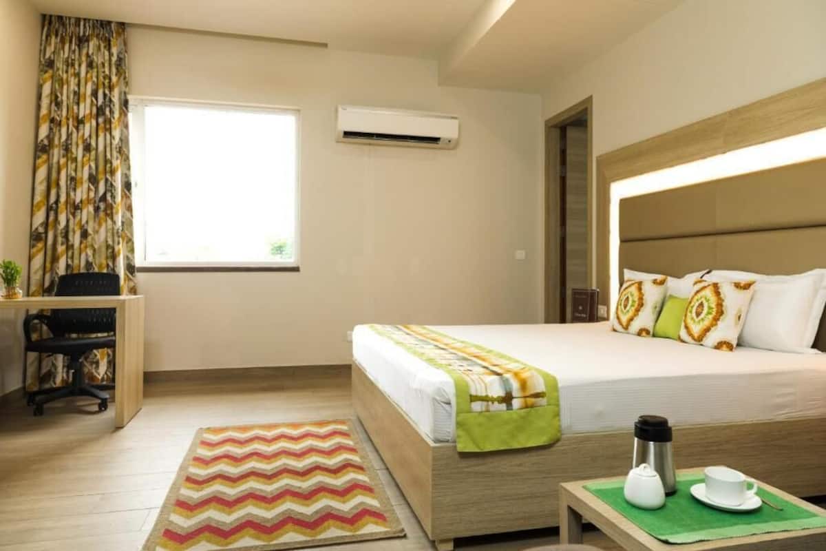 A hotel room with a bed, desk, chair, and a window with curtains.