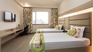 A hotel room with two beds, a desk, a TV, and a window with curtains. - SILVER OAK (Gurugram)
