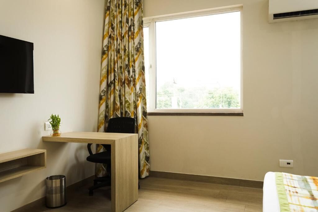 A small, well-lit room with a desk, chair, and a bed.