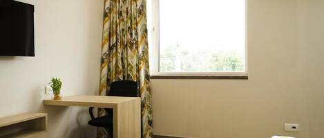 A small, well-lit room with a desk, chair, and a bed.