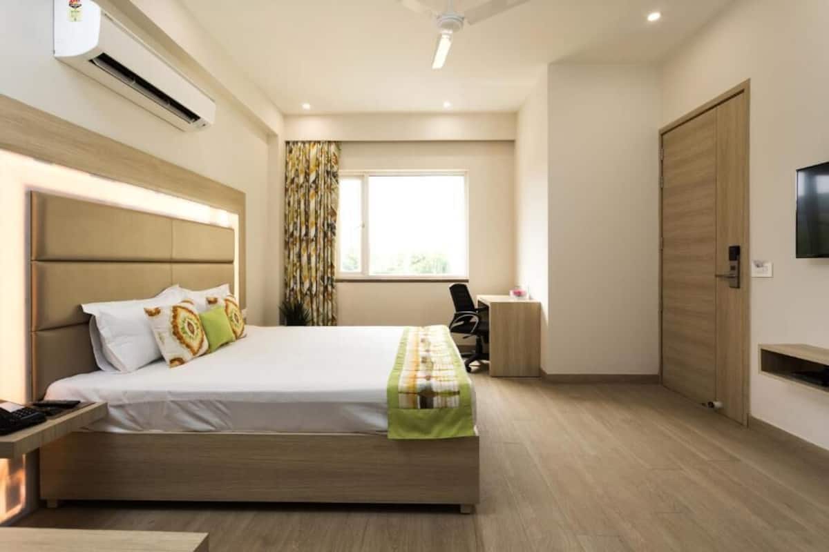 A modern hotel room with a large bed, a desk, a chair, a TV, and a wardrobe.