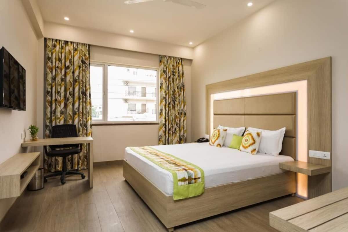 A modern hotel room with a bed, desk, chair, and a large window with curtains.