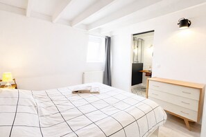 Een slaapkamer met een bed, nachtkastje, dressoir en een badkamer zichtbaar door een open deur.