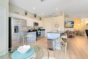 A modern kitchen with stainless steel appliances, a dining area with a glass table, and a living space with a TV and seating. - Four Bed Pool/Spa Home in Windsor Palms Resort (Kissimmee)