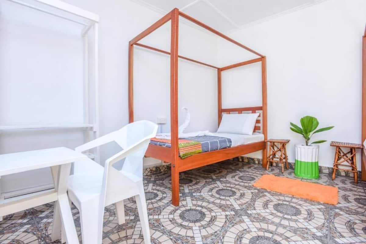 Un lit à baldaquin avec un cadre en bois, une chaise blanche, une petite table et une plante en pot.