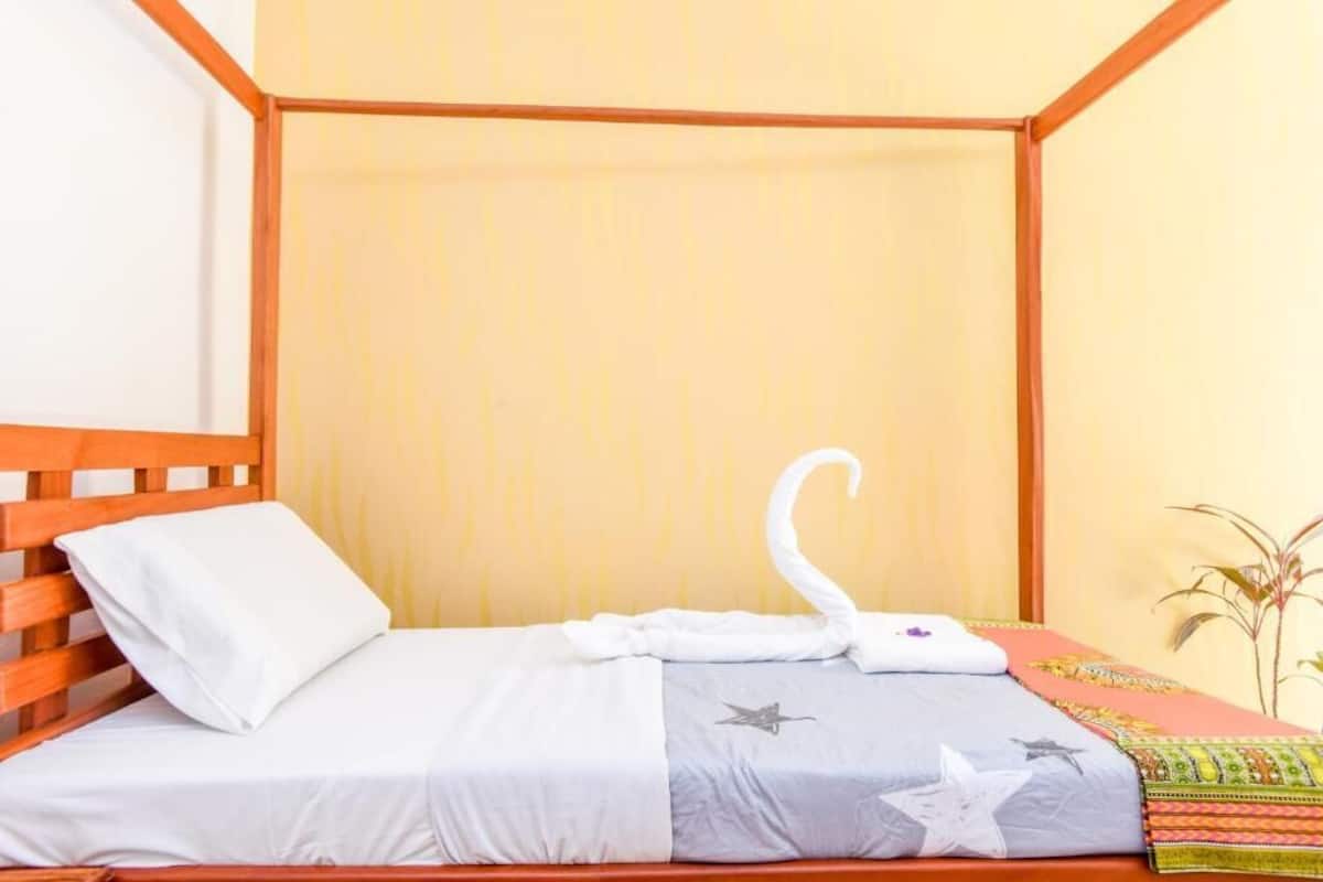 Un lit à baldaquin avec une couvre-lit blanche et grise, un oreiller blanc et une serviette blanche pliée sur le lit.