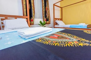 Ein Zimmer mit zwei Betten, eines mit einem gemusterten Bettbezug und das andere mit einem schlichten, blauen Bettbezug.