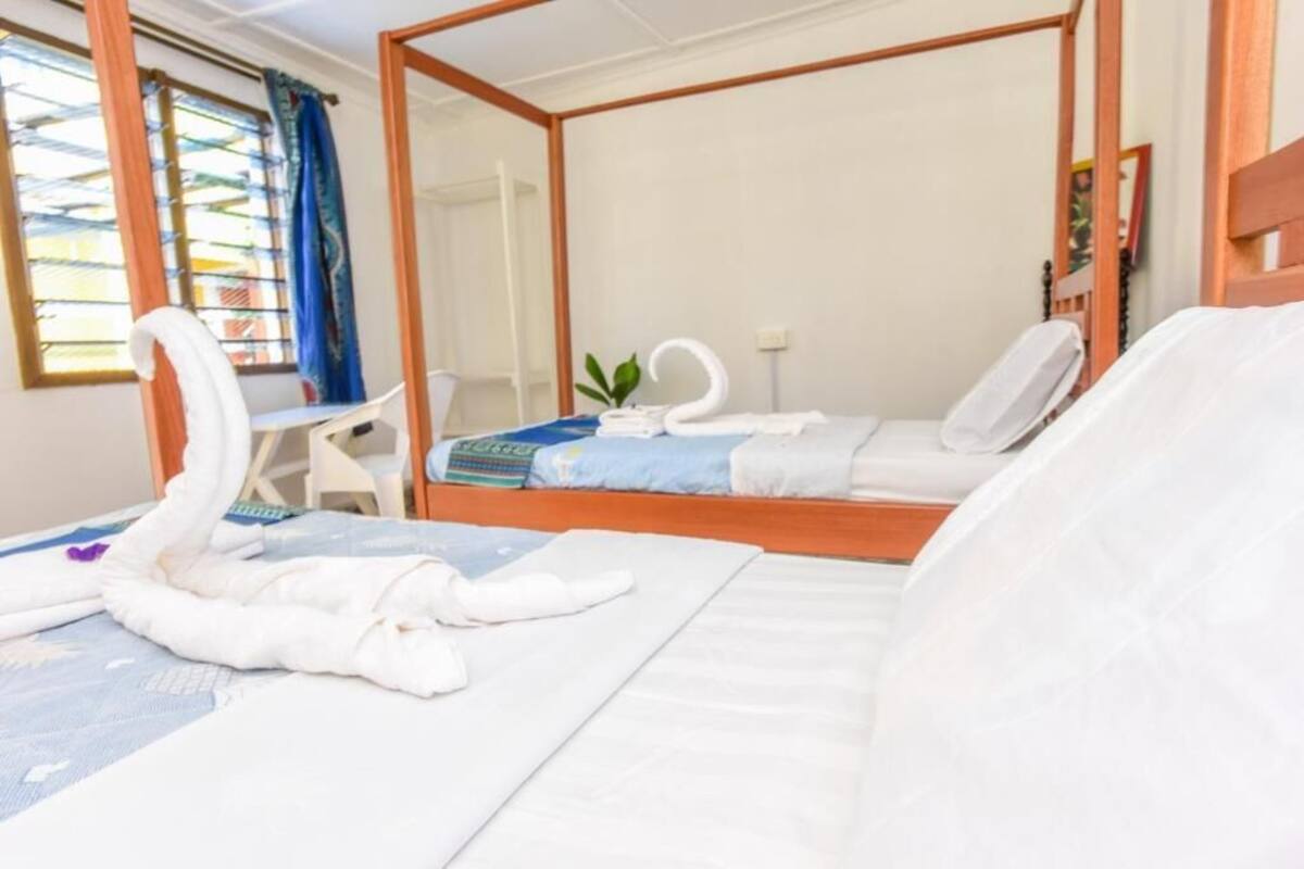 Un lit à baldaquin avec du linge de lit blanc et un coussin bleu. On y trouve une petite table avec une plante et une serviette pliée.