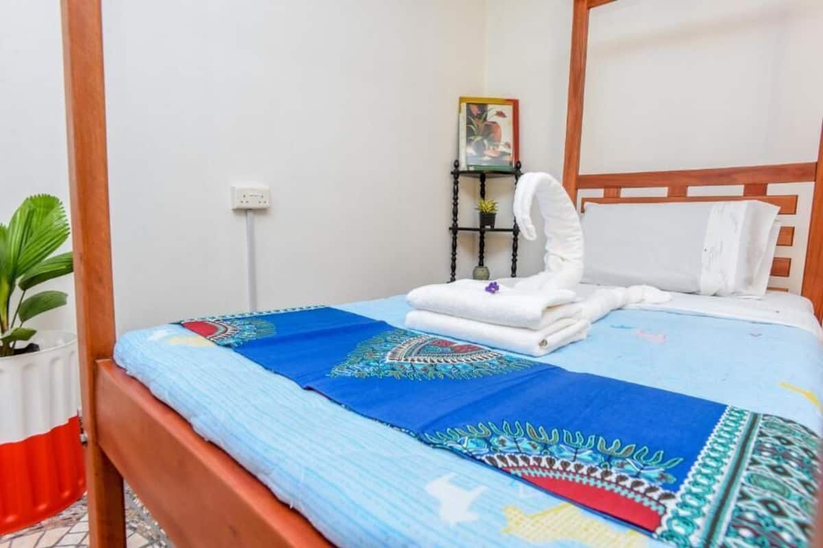 Un lit bien fait, recouvert d’une couvre-lit à motifs bleus et blancs, avec un oreiller blanc et une serviette blanche pliée posée sur une tête de lit en bois.