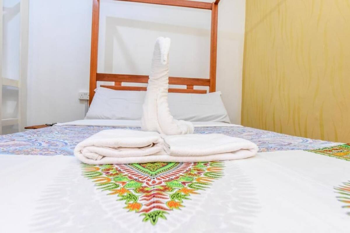 Un lit bien fait, avec une serviette blanche pliée au centre, une tête de lit en bois et une couvre-lit aux couleurs vives.