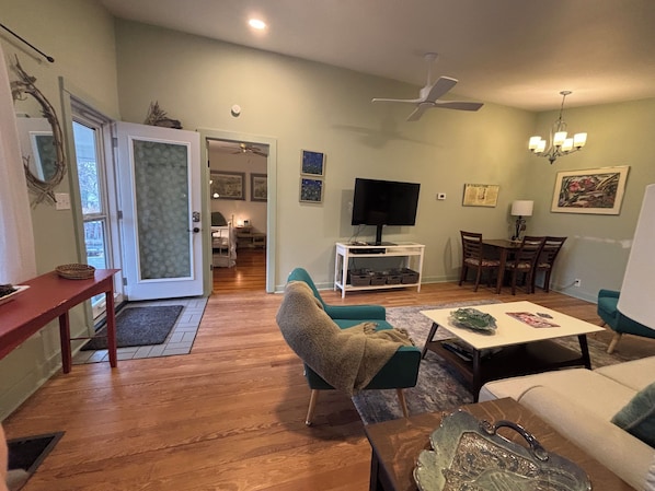 Uma sala de estar com televisão, área de refeições e corredor que dá para outro quarto.