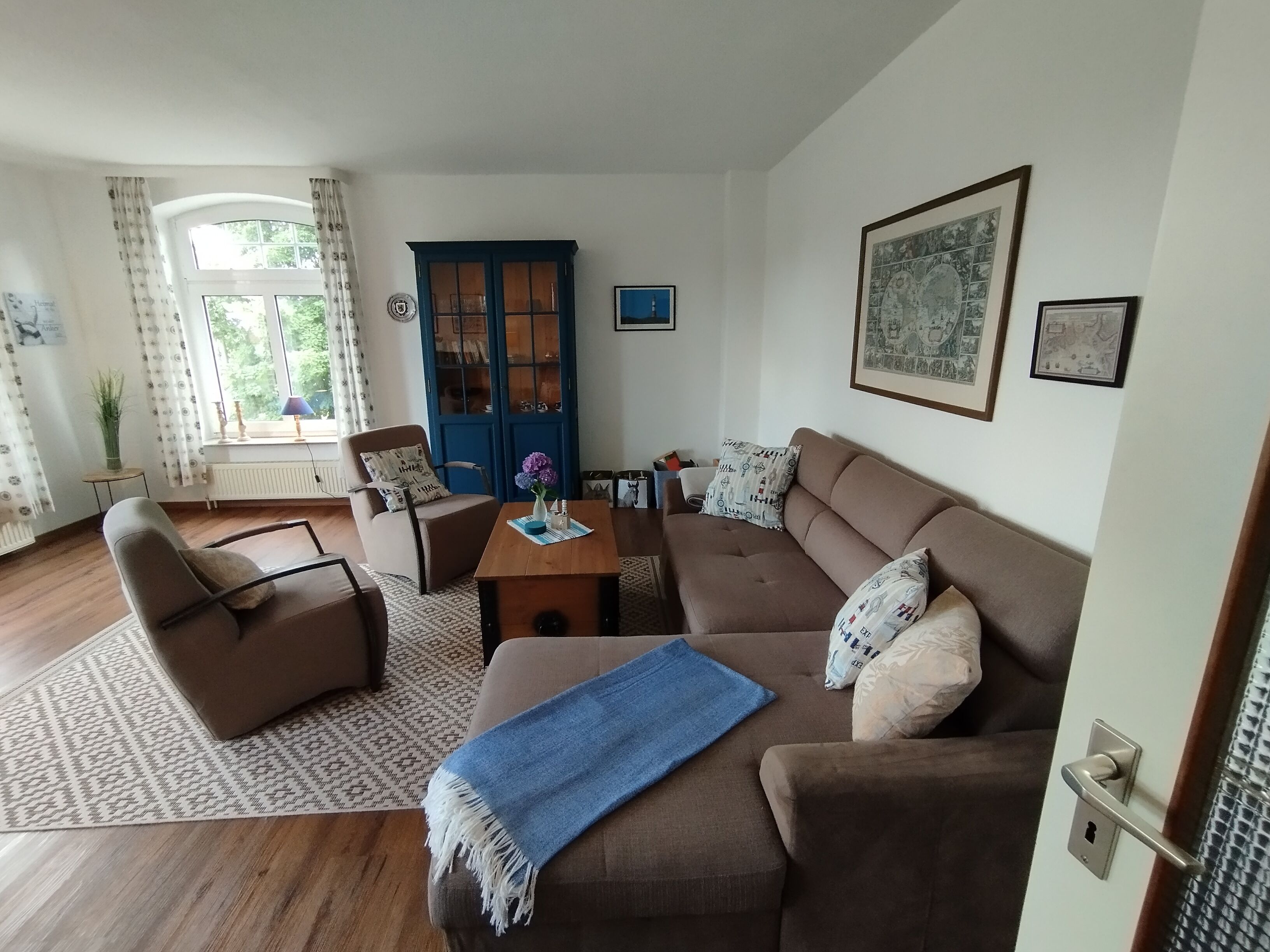 A living room with a brown sofa, a blue armchair, a wooden coffee table, and a blue throw blanket.