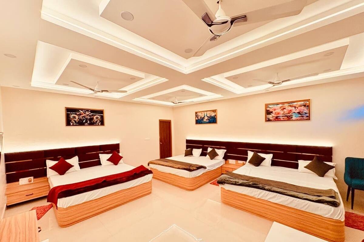 A modern hotel room with three beds, a ceiling fan, recessed lighting, and artwork on the walls.