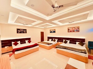 Una camera d'albergo moderna con tre letti, una ventola a soffitto, illuminazione a incasso e opere d'arte alle pareti.