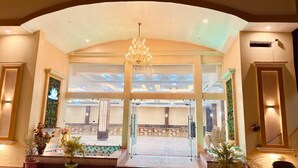 A grand entrance with a chandelier, a reception desk, and a view into a spacious hall with seating. - Amber Palace (Faizabad)