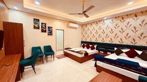 A hotel room with a bed, two chairs, a desk, and a ceiling fan. - Amber Palace (Faizabad)