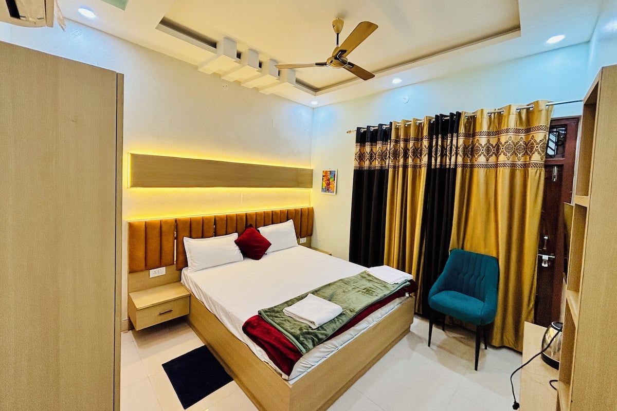 A modern bedroom with a bed, bedside table, chair, ceiling fan, and curtains.