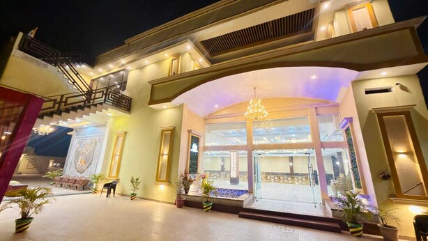 A hotel entrance with a grand staircase, a chandelier, and potted plants. - Amber Palace (Faizabad)
