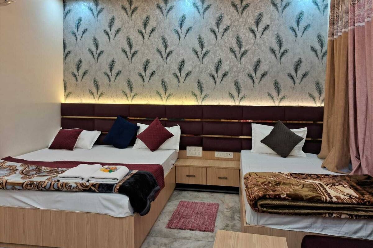 A bedroom with a patterned wallpaper, a headboard, two beds with pillows, a bedside table, and a nightstand.