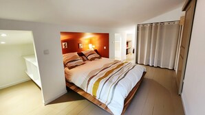 A bedroom with a bed, a nightstand, a wall-mounted lamp, and a window with curtains. - Pool and spa villa by the lake (Sanguinet)