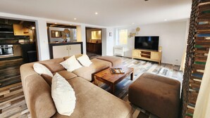 A modern living room with a sofa, a coffee table, and a TV. There is a kitchen area with cabinets and a countertop. - Pool and spa villa by the lake (Sanguinet)