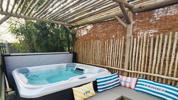 A hot tub with a wooden deck, a pergola overhead, and a bamboo fence. - Pool and spa villa by the lake (Sanguinet)