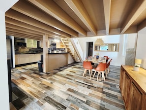 A modern kitchen with wooden cabinets, a dining area with a wooden table and chairs, and a staircase leading to another level. - Pool and spa villa by the lake (Sanguinet)