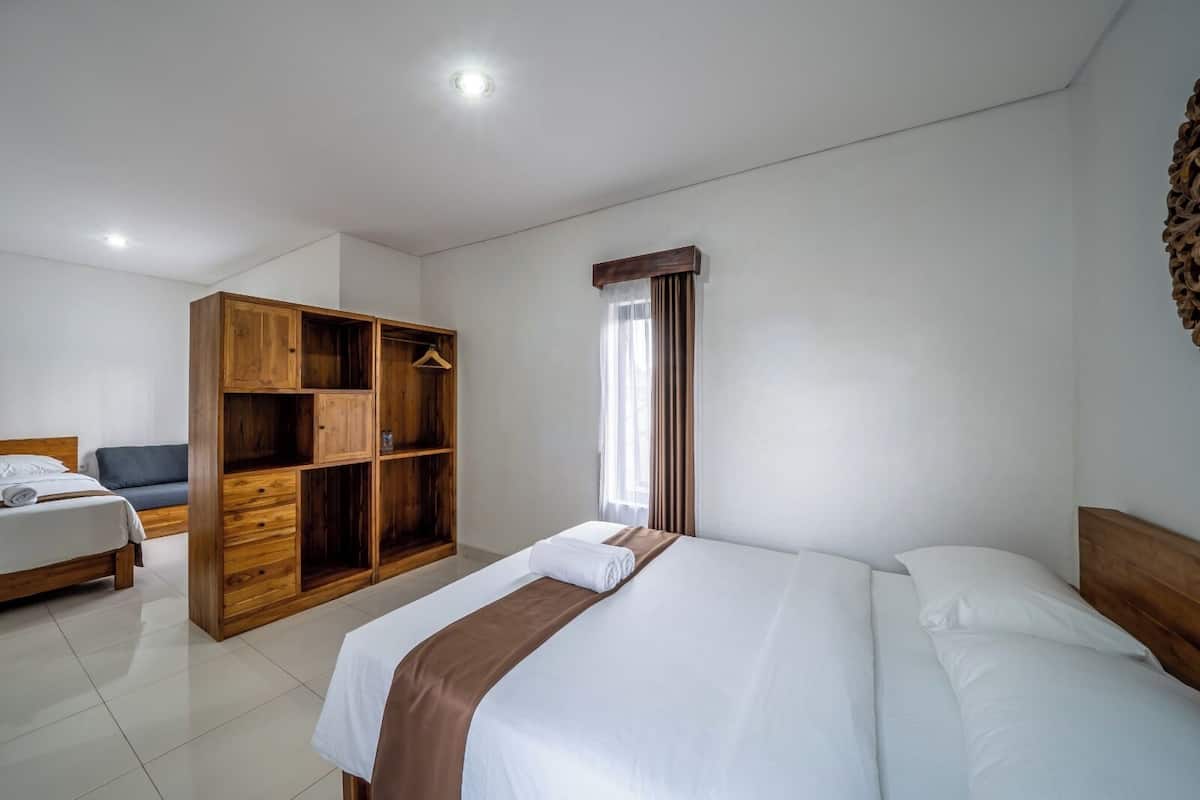 A hotel room with a bed, a wooden wardrobe, a chair, and a window with curtains.