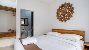 Una camera da letto con un letto in legno, un comodino in legno, un elemento decorativo a parete e un bagno visibile attraverso una porta aperta.