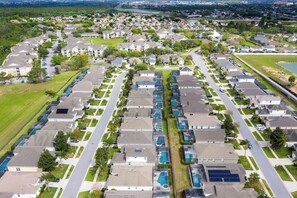 An aerial view of a residential area with rows of houses, a central road, and a body of water in the background. - Amazing Disney Dream Getaway in Windsor Palms Resort! (Kissimmee)
