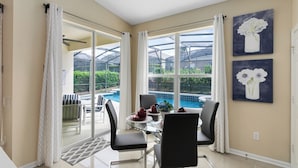 Ein Essbereich mit einem Glastisch, schwarzen Stühlen und Blick auf einen Pool und Grünflächen.