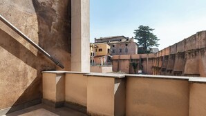 A balcony with a concrete wall, a metal railing, and a view of buildings in the background. - Large 6-Bed Stay near the Colosseum (Rome)