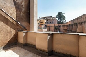 Ein Balkon mit einer Betonwand, einem Metallgeländer und Blick auf Gebäude im Hintergrund.