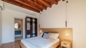 A bedroom with a wooden ceiling, a bed with white bedding, a nightstand, and a built-in wardrobe with a mirror. - Large 6-Bed Stay near the Colosseum (Rome)