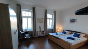Ein Schlafzimmer mit einem großen Bett, zwei Fenstern, einem Sessel und einer Heizung.