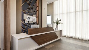 Un mostrador de recepción de diseño moderno, un letrero que indica que es un Holiday Inn Express & Suites, y un ventanal con cortinas traslúcidas.