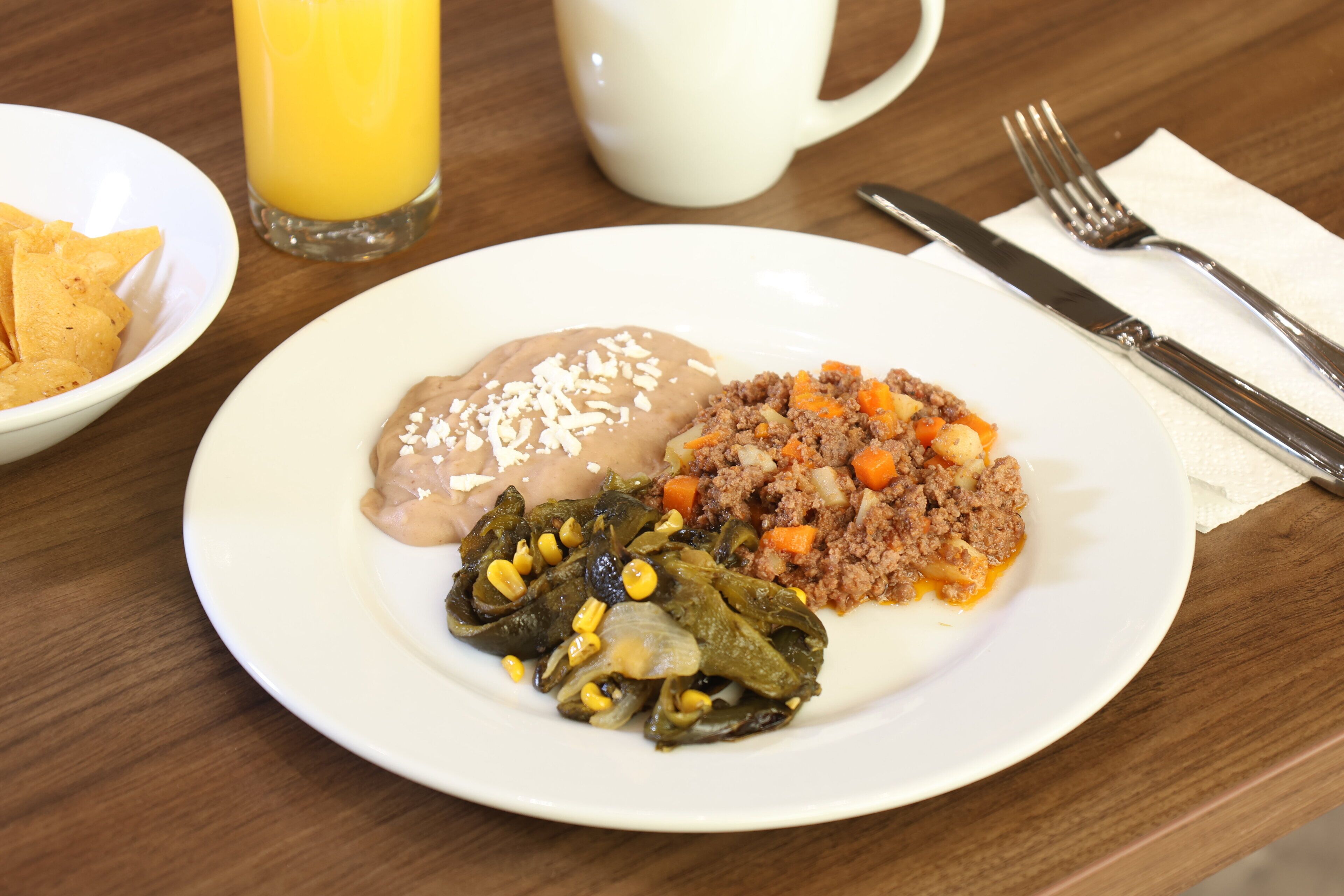 A plate of food with a glass of orange juice, utensils, and a napkin on a wooden table.
