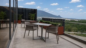 Un balcón con mobiliario exterior, vista a una montaña y un paisaje urbano al fondo.