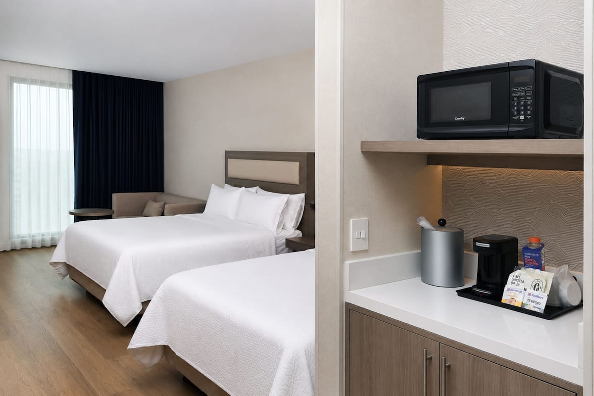 A hotel room with two beds, a coffee maker, a microwave, and a small table with a coffee pot and a bag of coffee.