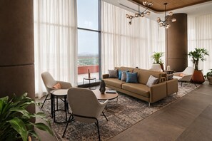A modern living room with a sofa, chairs, a coffee table, and a view of the city through large windows. - Holiday Inn Express and Suites Monterrey Sendero by IHG (Escobedo)