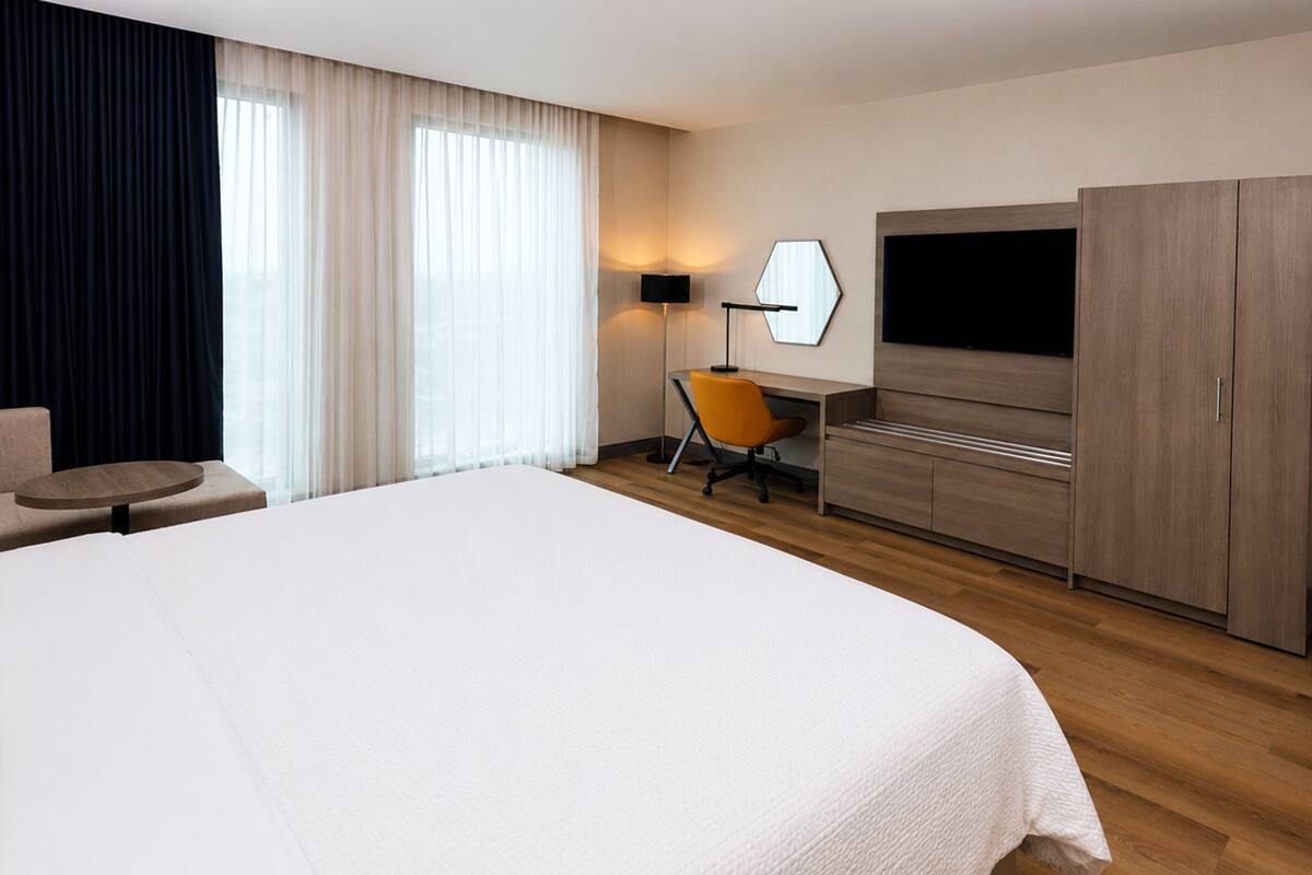 A hotel room with a large bed, a desk with a chair, a TV, and a wardrobe.
